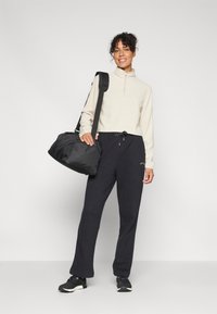 Pullover grigio chiaro con zip, pantaloni della tuta neri, sneaker nere e borsa a tracolla nera. Vestibilità comoda e texture morbida, con vita regolabile.