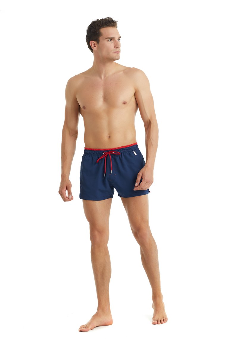 Tummansininen uimalohko punaisella nauhalla, joustava vyötärö, sivutaskut ja sileä, kevyt kangas. Ei lisäkuvioita tai logoja.