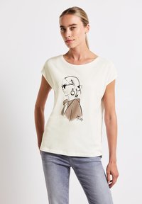 Camiseta de algodón color crema con mangas cortas que presenta un dibujo en línea negra de una mujer con gafas de sol y pendientes, con acentos en color marrón claro.