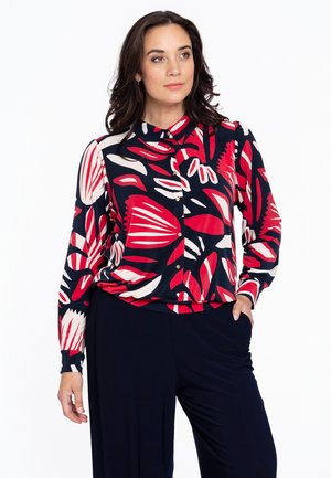 Blouse à imprimé floral en bleu marine, rouge et blanc. Manches longues, devant boutonné, col montant. Assorti avec un pantalon bleu marine foncé. Texture de tissu lisse.