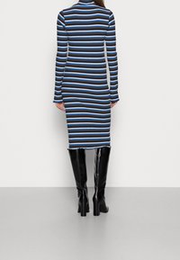 Svart och blå randig ribbad klänning med långa ärmar och en figurnära silhuett, med fransar i nederkant och hög krage.