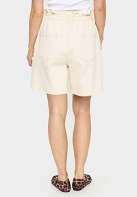 Shorts en coton beige avec un waistband élastique, dotés de deux poches arrière et d'une coupe décontractée, se terminant au-dessus des genoux.