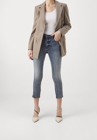 Béžové sako přes bílý top, doplněné o zkrácené modré džíny a krémové lodičky na špičce s černými kotníkovými pásky.