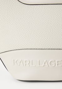 Torba od teksturirane bijele kože s crnim akcentima, s istaknutim urezanim logom "KARL LAGERFELD" i strukturiranim oblikom.