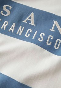 Pamučna majica s horizontalnim plavim i bijelim prugama, s natpisom "SAN FRANCISCO" izvezenim bijelom bojom na plavoj traci.