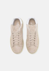 Zapatillas de ante beige con acentos de cuero blanco, puntera redonda, cordones planos y suela de goma texturizada. Incluye la marca en la lengüeta.