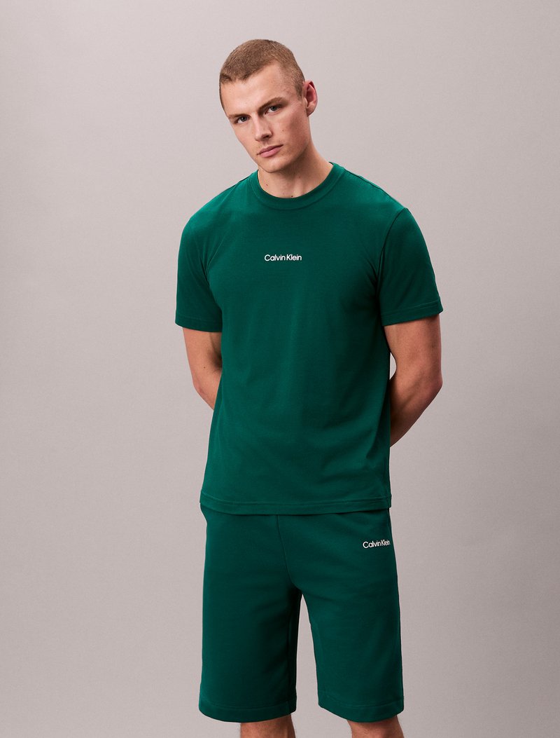 Ensemble t-shirt et shorts en coton vert, avec un col rond et un logo "Calvin Klein" brodé. Texture douce, coupe décontractée, manches courtes.
