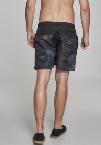 Shorts de bain camouflage noirs et gris avec une taille élastique et une poche à fermeture éclair à l'arrière, fabriqués en tissu léger et résistant à l'eau.