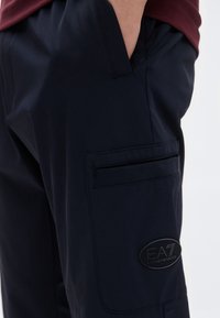 Σκούρο μπλε παντελόνια φόρμας από ύφασμα με λεία υφή, με πλαϊνή τσέπη και κυκλικό μαύρο λογότυπο στον μηρό.