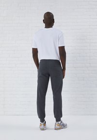 Herrenoutfit bestehend aus einem schlichten weißen Baumwoll-T-Shirt und dunkelgrauen Fleece-Jogginghosen mit elastischem Bund, kombiniert mit silbernen und orangen Sportschuhen.