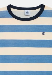 Gestreiftes T-Shirt mit abwechselnd hellblauen und cremefarbenen Streifen, einem navyfarbenen Rundhalsausschnitt und einem kleinen navyfarbenen Logo auf der Brust. Hergestellt aus weicher Baumwolle.