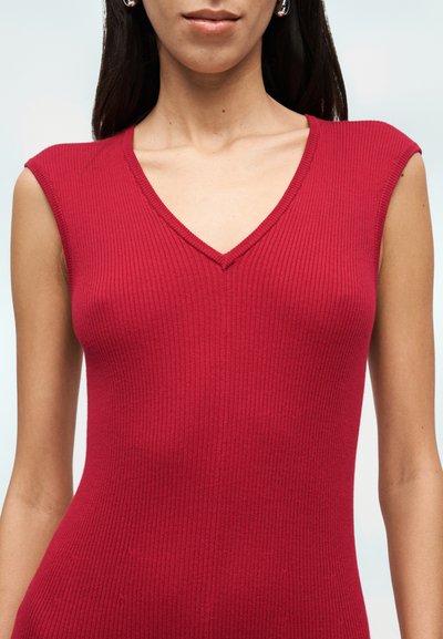 Κόκκινο πλεκτό αμάνικο τοπ με ριγέ υφή, σε σχήμα V στη λαιμόκοψη και υφασμάτινη υφή, παρουσιάζοντας εφαρμοστή σιλουέτα. Μινιμαλιστικός σχεδιασμός με καθαρές γραμμές.