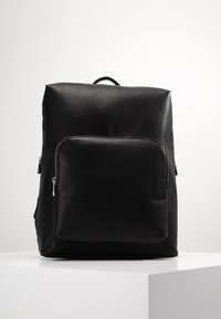 Svart läderryggsäck med en slät yta, rektangulär form, ett bärhandtag och en framfick med dragkedja. Minimalistisk design utan synliga logotyper.