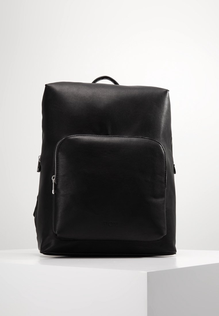 Svart läderryggsäck med en slät yta, rektangulär form, ett bärhandtag och en framfick med dragkedja. Minimalistisk design utan synliga logotyper.