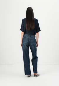 Donkerblauwe jeans met een losse fit, voorzien van een klassieke vijfzakkenontwerp en subtiele stiklijnen. Gecombineerd met een gestructureerd zwart topje.