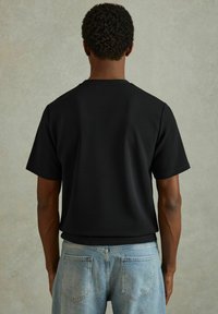Cămașă neagră cu mânecă scurtă, dintr-un material texturat, cu guler tip crew neck. Asortată cu blugi din denim de un albastru deschis, cu buzunare în spate.