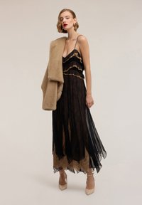 Abito lungo in pizzo nero con dettagli arricciati, sovrapposto a tessuto color nudo. Completato da uno scialle di pelliccia beige e scarpe con tacco color nudo.