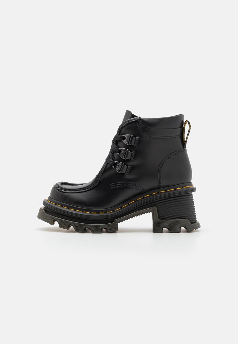 Bottine noire en cuir avec semelle crantée épaisse, talon épais, trois crochets métalliques pour les lacets et surpiqûres jaunes autour de la semelle.