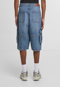 Bermudas de mezclilla en azul claro con un ajuste relajado, múltiples bolsillos frontales y laterales, y una etiqueta en la cintura. Dobladillo estructurado y diseño casual.