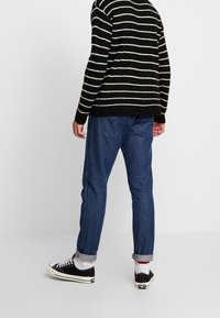 Czarnobiały sweter w paski, dzianinowy, luźny fason, zestawiony z niebieskimi dżinsami, podwiniętymi mankietami i czarnymi trampkami z białymi podeszwami.