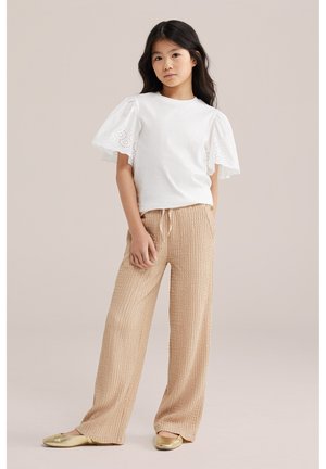 Meitene ar gariem tumšiem matiem, valkājot baltu blūzi ar pūstām izšūtām piedurknēm, bēša faktūras platām biksēm un zeltainām plakanām kurpēm, stāv nekustīgi.