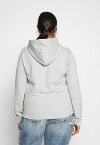 Sudadera gris con capucha ajustable, puños y dobladillo acanalados, fabricada en un tejido suave, combinada con unos jeans azules desgastados de corte relajado.