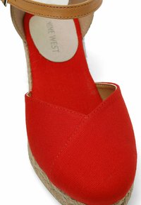 Wedge espadrille in tela rossa con cinturino alla caviglia color beige e suola in juta. Presenta un design frontale incrociato. Rivestimento interno liscio con logo.