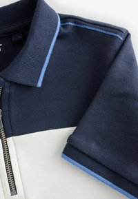 Tumesinine ja valge polo särk, millel on lukuga kaelus, tekstureeritud krae ning sinised aktsendid varrukate servades.