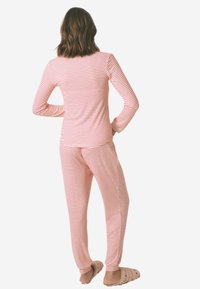 Rød og hvidstribet pyjamashirt med lange ærmer, parret med matchende stribede bukser, blødt materiale og rummelig pasform. Lyse slippers.