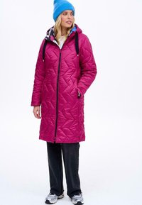 Fuchsie prošívaný dlouhý kabát s kapucí, se zapínáním na zip a šňůrkou. Spárovaný s černými kalhotami a modrým pleteným čepičkou.