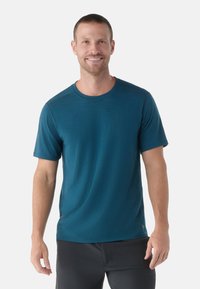 Camiseta de manga corta y cuello redondo en azul teal, hecha de una tela suave con una textura sutil, combinada con pantalones deportivos negros.