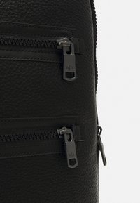 Zwarte leren rugzak met een textuur oppervlak, dubbele ritszakken en metalen hardware met gegraveerde merkaccenten.