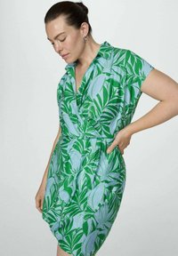 Rochie cu mânecă scurtă dintr-un material bleu deschis, cu imprimeu cu frunze verzi, având un guler la gât și talie strânsă cu fustă largă.