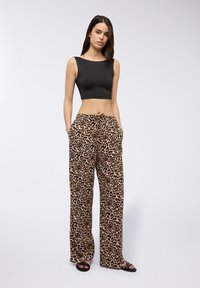 Top cropped nero e pantaloni larghi beige con stampa leopardata e tasche; texture liscia, dettaglio con cordoncino e sandali neri piatti.