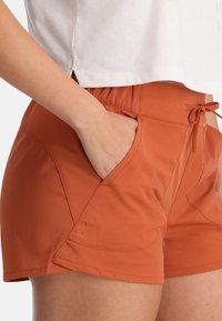 Oranje sportshorts met een tailleband met trekkoord, zijzakken en een gladde textuur. Bevat een subtiele logo-in-het-stof geperst.