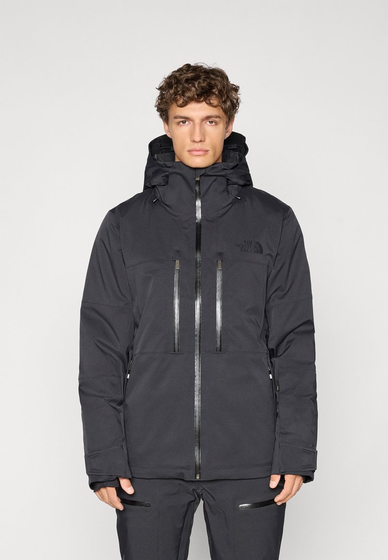 Giacca nera impermeabile con colletto alto, cappuccio regolabile e due tasche sul petto. Caratterizzata da chiusure con zip e dettagli con logo.