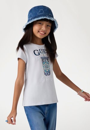 Camiseta blanca con gráfico azul y acentos bordados, combinada con un sombrero tipo bucket de mezclilla con bordes deshilachados en azul claro y patrones de corazones.