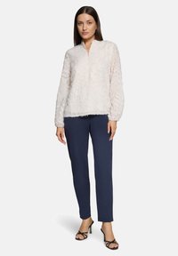 Hellrosa strukturiertes Oberteil mit rundem Ausschnitt und langen Ärmeln, kombiniert mit schlanken marineblauen Hosen und schwarzen, Riemchen-High Heels.