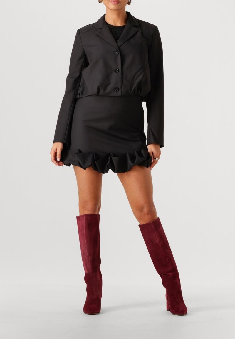 Zwarte cropped blazer met drie knopen, gelaagde zwarte minirok met geruchte zoom en kniehoge bordeauxrode suède laarzen.