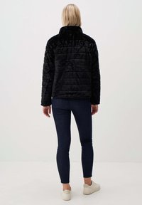 Zwarte faux fur jas met een hoge kraag en gequilt textuur, gecombineerd met donkere spijkerbroek en lichtgekleurde sneakers.