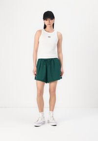Weißes Tanktop mit "GAP"-Logo, grüne Shorts mit Kordelzug und weiße High-Top-Sneaker. Schwarze Haube auf dem Kopf. Einfache, legere Outfit.
