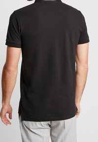 Polo noir en coton lisse, avec des manches courtes et un col classique. Fentes latérales à l'ourlet pour faciliter les mouvements.