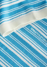 Blauw-wit gestreepte gebreide stof met geribbelde witte boord en "CREATIVE STUDIO" geborduurd in witte draad.