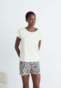 Ljus beige bomulls T-shirt med korta ärmar, parat med svart och vit zebrarandig shorts. Enkelt mönster och mjuk textur.