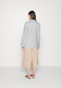 Blazer de linho cinza claro com mangas longas, racha única nas costas, combinado com calças de perna larga bege e sandálias castanhas.