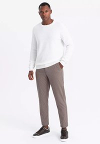 Biały sweter o fakturze z długimi rękawami w połączeniu z brązowymi spodniami w kratę i ciemnymi sneakersami, charakteryzujący się slim fit oraz bocznymi kieszeniami.