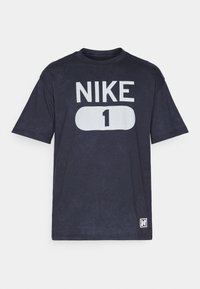 T-shirt noir à manches courtes en tissu avec une finition légèrement texturée. Présente un grand graphique blanc avec "NIKE" et "1" au centre.