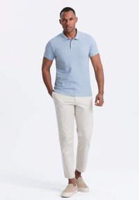 Vaaleansininen polo-paita, jossa on kaulus ja lyhyet hihat, yhdistetty beigeihin slim fit -housuihin ja beigeihin liukuvahihoihin kenkihin. Yksinkertainen, siisti muotoilu.