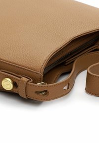 Tummanruskea teksturoitu nahkainen olkalaukku, jossa säädettävä olkahihna, kultainen nappidetalji ja näkyvä musta vetoketjutaskun avaus.