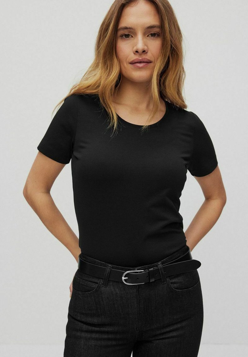 Czarna koszulka z krótkim rękawem z gładkiego materiału z okrągłym dekoltem, w połączeniu z ciemnoniebieskimi dżinsami i czarnym paskiem z srebrną klamrą.